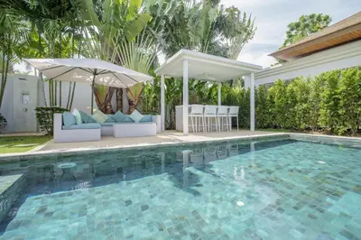 a swimming pool with chairs and an umbrella at Stylish 3BR Pool Villa trichada Airport Shuttle in Phuket Town