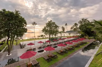 a row of tables with red umbrellas next to a pool at The Vijitt - Deluxe Villa in Ban Saiyuan (1)