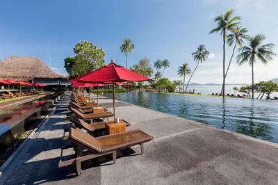 a row of chairs and umbrellas next to a body of water at The Vijitt - Deluxe Pool Villa in Ban Saiyuan (1)