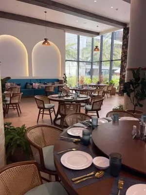 a restaurant with tables and chairs in a room with windows at Kora Beach Studio in Layan Beach
