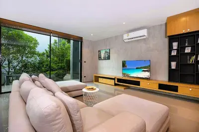 a living room with a couch and a tv at Nature-Inspired 2BR Duplex P12 with pool and gym in Kamala Beach