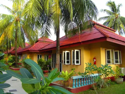 a yellow house with a red roof and palm trees at Palm Village in Rawai Beach