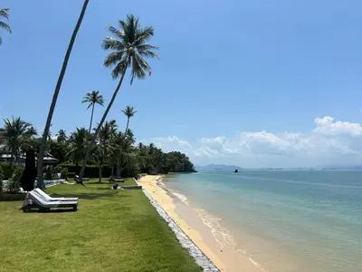a beach with palm trees and the ocean on a sunny day at Coastal Escape Koh Yao Noi in Ko Yao Noi