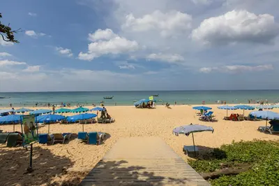 a beach with many blue umbrellas and people on it at Spacious studio with access to the pool in Karon Hill condo in Karon Beach