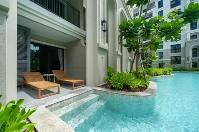 a swimming pool with two chairs and a table next to a building at Apartments 15 minutes walk from Bangtao Beach with a cinema in Phuket