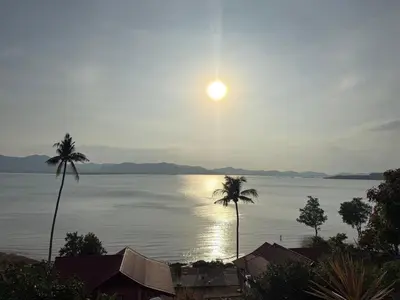a view of the water with palm trees and the sun at The Good View Koh Yao Noi in Ko Yao Noi