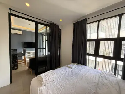 a bedroom with a white bed and large windows at Palmyrah Surin Apartments by Mill in Surin Beach