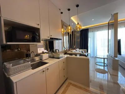 a kitchen with white cabinets and a living room at Bangtao new studio in Bellevue Lagoon in Laguna Phuket