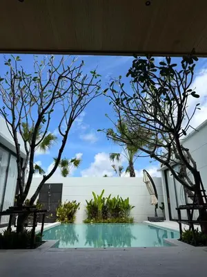 a swimming pool with trees and a white wall at Phuket Moana Pool Villa in Ban Na Nai