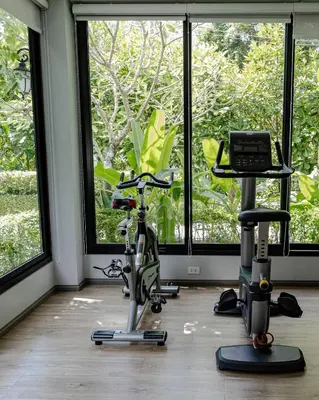 a room with a gym with a exercise bike and windows at Cozy studio Pool View near of NaiYang beach in Nai Yang Beach