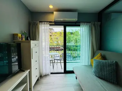 a living room with a couch and a tv and a balcony at Comfy studio - 10 min walk to NaiYang Beach in Nai Yang Beach