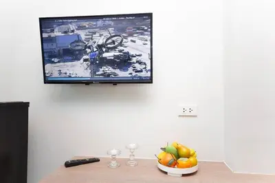 a television on a wall with a bowl of fruit on a table at Cozy Bonaparte Studios in Ban Thalat Choeng Thale