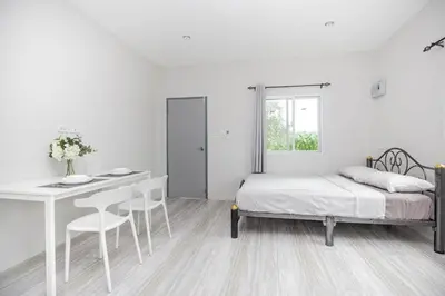 a white bedroom with a bed and a table and chairs at VISUT apartments near mountain in Ban Thalat Choeng Thale