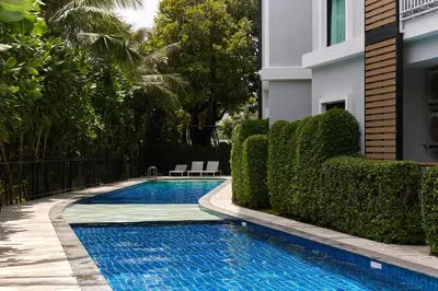 a swimming pool next to a building with bushes at Cozy Apartment at Rawai with Pool Access in Phuket Town