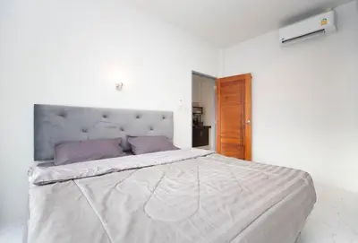 a white bedroom with a large bed with purple pillows at Lovely OPTIC apartments on Bang Tao Beach in Ban Thalat Choeng Thale