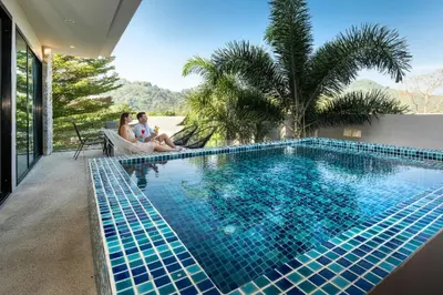 a couple sitting on a chair next to a swimming pool at Duplex Villa Natural Touch A2 2BR with scenic view and rooftop terrace in Kamala Beach
