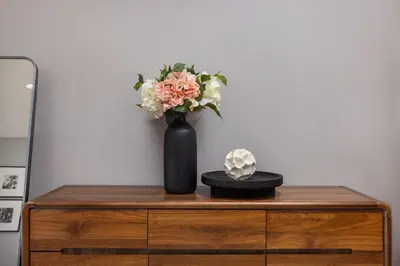a black vase with flowers on top of a dresser at Oliva 1BR Suite — The Title Legendary BangTao in Bang Tao Beach