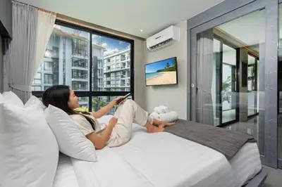 a woman sitting on a bed looking at her cell phone at Deluxe 1BR Pool view 58SQM in Kamala Condo Citygate P302 in Kamala Beach
