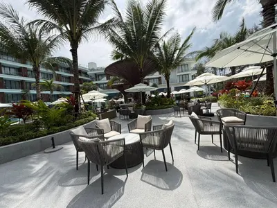 a patio with tables and chairs and palm trees at Sunshine BEACH FRONT in Layan Beach