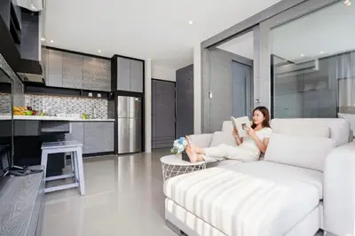 a woman sitting on a couch reading a book at 1BR Mountain View Condo Citygate P708 in Kamala Beach