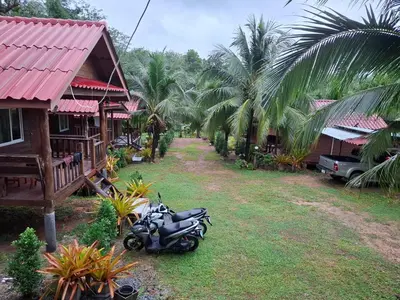 a motorcycle parked next to a house with palm trees at Fadel Bungalow ฟาดิลบังกะโล in Ban Lo Pa Ret
