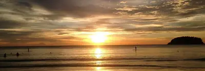 a sunset on the beach with people in the water at The Seaview Kata in Kata Beach
