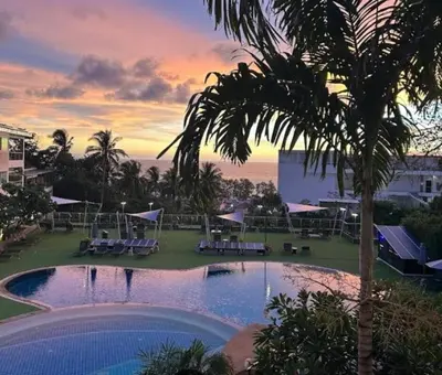 a resort pool with a palm tree and a sunset at Modern 2BR Condo at Karon Butterfly Phuket in Karon Beach