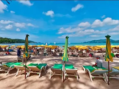 a man sitting on a beach with chairs and umbrellas at Studio Bangla Suite 304 in Patong Beach