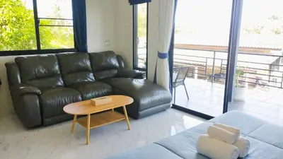a living room with a black leather couch and a table at Leamsai Whisper Home in Thalang