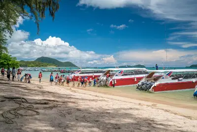 a group of people walking on a beach next to boats at Rawayana West Villas & Kids Park in Rawai Beach