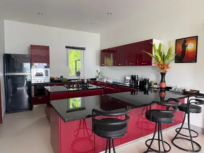 a kitchen with red cabinets and black bar stools at Sunset bay view villa krabi in Ban Khao Thong
