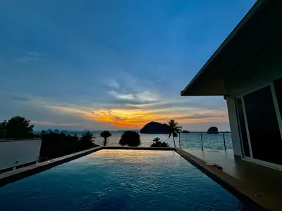 a swimming pool in front of a house with a sunset at Sunset bay view villa krabi in Ban Khao Thong