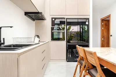 a kitchen with white cabinets and a table with chairs at 3BR Pool Villa JAAI in Ban Saiyuan (1)