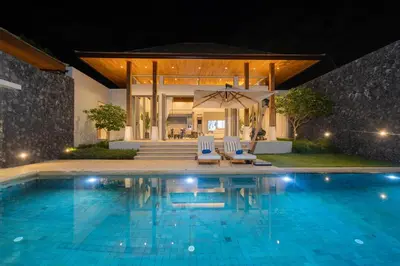 a pool at night with two chairs and an umbrella at Luxury Royale Bangtao Pool Villa with maid in Thalang