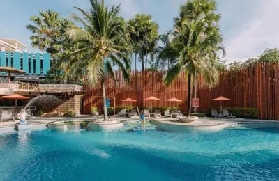a pool at a resort with palm trees and umbrellas at The Beach Condotel Kata in Kata Beach