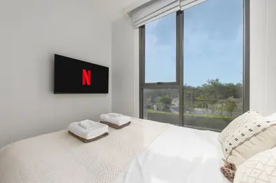 a bedroom with a large white bed with a tv on the wall at Melia 2BR with Rooftop Pool - Skypark Laguna in Laguna Phuket