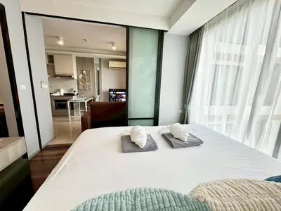 a bedroom with a large white bed with two towels at Stylish 1BR Surin Beach Kitchen & Rooftop Pool by Renttini in Ban Lum Fuang