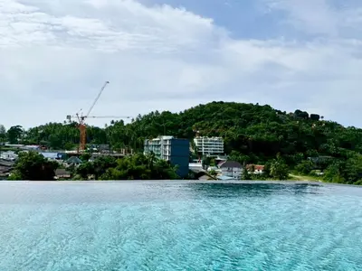 a large body of water with a hill in the background at Stylish 1BR Surin Beach Kitchen & Rooftop Pool by Renttini in Ban Lum Fuang