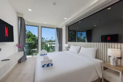 a bedroom with a large white bed and large windows at Suite Melos 2BR Pool Gym Access Ozone in Laguna Phuket