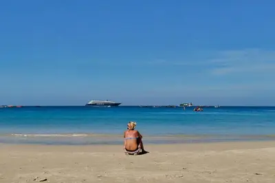 a woman sitting on the beach looking at the ocean at Aqua Maya Phuket in Patong Beach