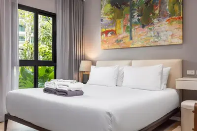 a bedroom with a white bed with a painting on the wall at Porto 1BR Pool Access Suite at Title Legendary in Bang Tao Beach