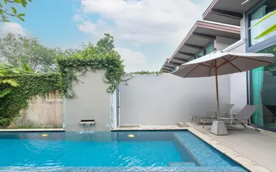 a swimming pool with an umbrella next to a house at Tropic Escape @ Baan Wana Phuket in Thalang