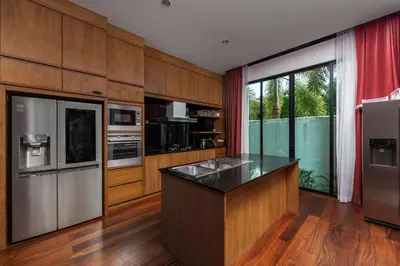 a kitchen with wooden cabinets and a refrigerator and a counter at Aroha Villa with Private Pool Near Nai Harn Beach in Rawai Beach