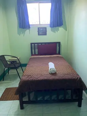 a bedroom with a bed with a brown blanket and a window at Rungtawan Hostel in Karon Beach