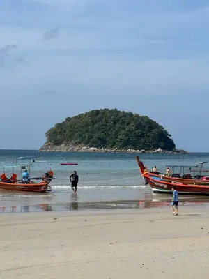 a group of people walking on the beach with two boats at KataKeet in Kata Beach