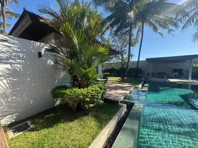 a swimming pool next to a house with a palm tree at Anchan Grand Residence Bangtao in Ban Pak Lak