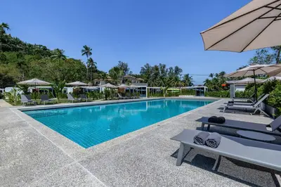 a pool at a resort with chairs and an umbrella at Apple House with Pool breakfast Surin Beach in Ban Lum Fuang