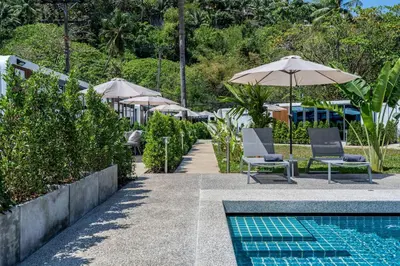 a pool with chairs and umbrellas next to a resort at Apple House Beach Access, Pool & Breakfast in Ban Lum Fuang