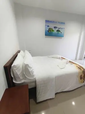 a bedroom with a bed with white sheets and a table at Airport Stay Phuket Zz in Nai Yang Beach