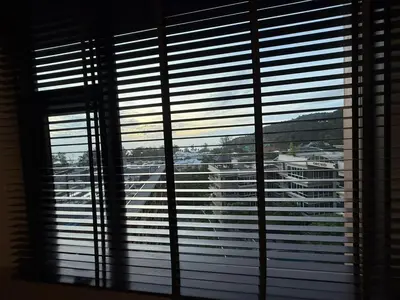 a window with a view of a city through the blinds at The Proud Karon Phuket - New 1BR Apartment 6floor in Karon Beach